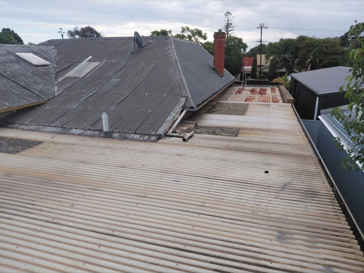 Faded old roof sheets with a dark roof and red brick chimney behind
